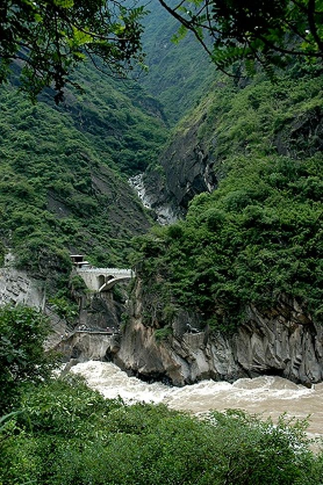 虎跳峡が一番狭くなった虎跳石のあたりを見下ろす。<br /><br />この峡谷の名の由来になったらしい虎の像が画像中央下の岩肌にポツリ。<br />この画像だとちょっと見つけにくいかも。<br /><br />轟々と流れ下る金沙江の水音が聞こえてくる。<br /><br /><br />あ、麗江市側には沢に橋も架かってるなあ。