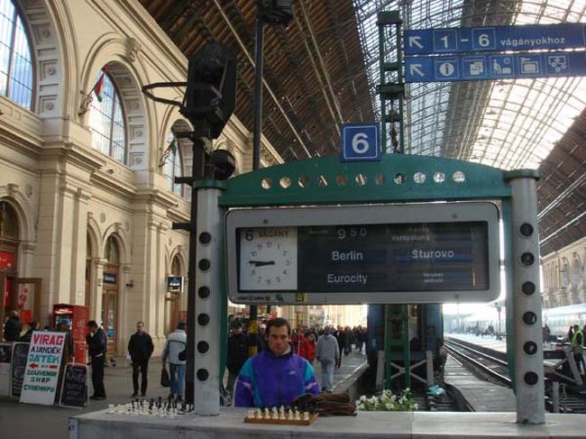 ←ブダペスト東駅<br />列車の案内板の前に、チェスの駒を並べた男性がいましたが、列車の待ち時間に一勝負する有料サービスでしょうか。