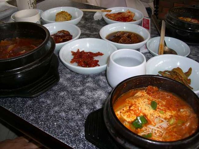 韓国のお通し<br /><br /><br />隣には友人の頼んだユッケジャン、机の上にはお通しのキムチ小皿がずらーっと並びます。