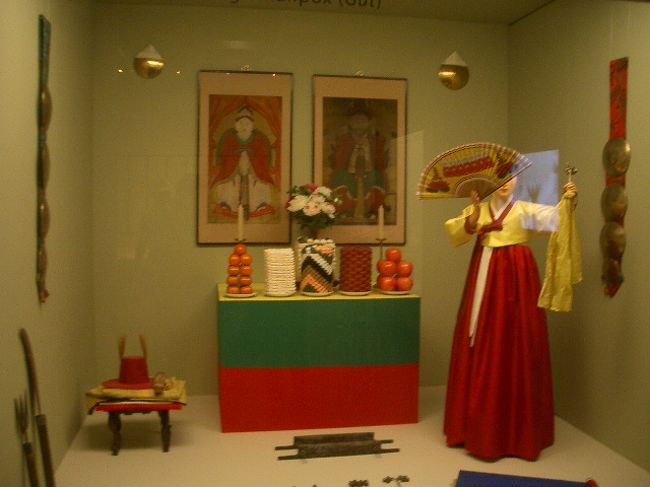 これ見たことある。<br />シャーマンの女性が、刀踏むやつ！<br /><br />黄色だし、細かい部分は違えど、この服装は巫女さんのコスと共通点を感じます。←コス違う・・<br /><br />韓国映画を観てると、なじみの「泣き女」とか、台湾の風俗を思わせる面もあるのですが、朝鮮半島の風土は、海外にいるという意識が飛んでしまうほど、違和感がなくなる瞬間があります。<br /><br />きっとその昔、朝鮮半島から日本に渡ってきた人たちも、いろんな事情はあったにせよ、似てっから居ついたんだろーなー。<br /><br />こういう展示を見ていると、アジアでは「白色」が、お葬式カラーであったのを思い出します。<br />日本も、いまじゃ結婚式に挑む女性は、ウエディング・ドレスはもちろん、神式でも純白の着物がメジャーですが、昔は黒い着物で結婚式をあげていたと、聞いたことがあります。<br /><br />つまり、めでたい時に黒を着ていたわけです。<br />逆に、白はお葬式に使う色。<br />台湾では、花粉症に使われるようなガーゼ・マスクに、白を使ってる人が驚くほど少ない。<br />柄モノ、派手派手プリントを着用しているのに、目を丸くした思い出があります。<br /><br />「みんな、派手すぎ！なんでだ、南だからか？アロハ風味？」<br /><br />って、びっくりしたけど派手なんじゃなくて、白くしてないだけだったんです。<br /><br />中国でも西安へ行った時、プリント・マスクの人が少なからず目に付きました。<br /><br />ちっちゃいんですけど。<br />そーゆう共通点を見つけると、なんだか地域的に繋がってる感じがして嬉しいです。<br /><br />