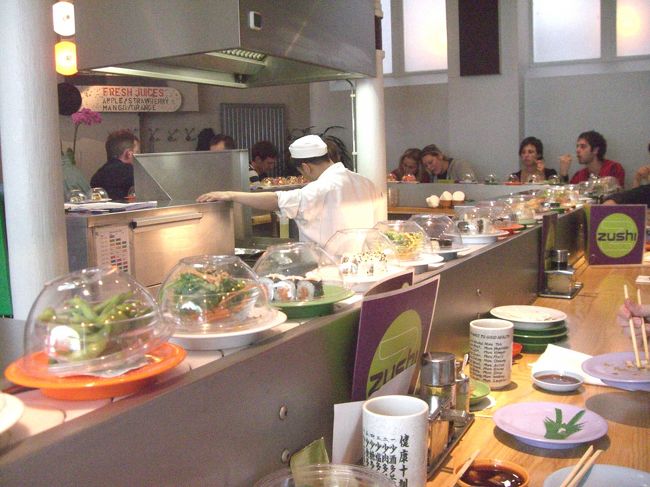 さて、オペラの前に腹ごしらえ。スキポール空港では寿司カウンターの前を決して素通りできない私。アムステルダムの散策の途中で目にした回転寿司屋さんもやっぱり素通りできませんでした。ムント塔近くの美しい運河沿いのお店で、何故かしらその店名は「ＺＵＳＨＩ」。私たちが席に座り、そうこうしているうち早々に満席となりました。<br />