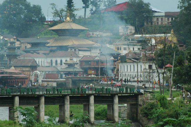 こちらは、カトマンズ市内と空港の中間地点くらいにあるネパール最大のヒンドゥー教寺院「パシュパティナート」です。ガンジス河の支流で聖なる川とされているバグナティ川の川岸にあります。<br />遠くからでも、煙があがっているのがみえますが、これは火葬しているため。観光客もかなり近くまで見に行けるそうですが、ワタクシは寄る気がしません。<br />荼毘に付されたあとは、この川に流されるのだとか。<br />ヒンドゥー教の人たちは墓を造らず、輪廻転生を信じているそうです。