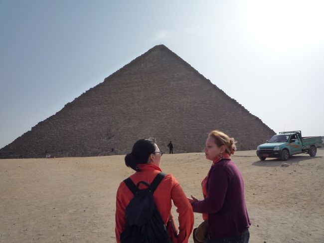 いよいよ、ギザのピラミッドへ移動。一番大きいクフ王のピラミッドは、午前と午後で中に入れる人数が各150名と決まっているようです。午後の入場チケットは、13時から販売開始。<br />朝7時にホテルを出発し、この13時の時点でお昼ご飯は食べていません。いつ食べるんだろう・・・？と疑問に思いつつ、クフ王のピラミッドへ。ガイドさんは、内部に入ることが出来ないので、外で一通り説明を受けてから、自由行動となります。<br />ちなみに、ガイドさん（右側の女性）は英語で説明してくれますが、USD50多く払うと日本語がしゃべれるエジプト人のガイドさんにすることも出来ました。