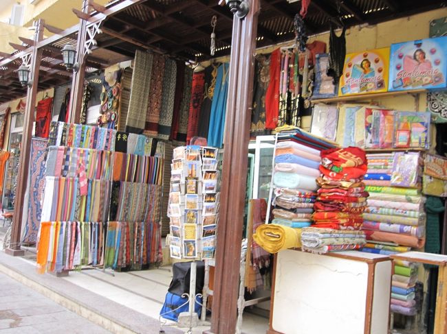 最初はわぁ〜い！買い物だあ〜！！<br />とドキドキしつつも、<br />お土産どれにしよっかなあ〜と楽しみで仕方がなかった私。<br />エキゾチックな布とか、エジプトらしい雑貨に胸がときめいていた。<br /><br />ただ、すべて値段表記されておらず交渉なのだ。<br />バトル慣れしていない甘〜い私にできるんだろうか？<br /><br />（ここからネガティブ・オーラが出ちゃうので、嫌な人は飛ばして下さいネ）<br /><br /><br />そしてバトルは始まったものの、添乗員さんの言った通り、どこに行っても最初からかなり高額な値段をふっかけられる。<br /><br />自分の場合、女一人だからなのか、<br />幼くみえたのか、完全になめられており、<br />買いたいものの値段が適度に下がるまでに<br />１品につき１０分〜３０分はかかる始末…<br /><br />関係ないけど、店のおじさん達は、<br />皆、いちいち顔が近いんだコレが！（笑）<br />そして強引なのは皆同じで、<br />ひどい時には「いらない」と言っても腕をつかまれ<br />店の奥に引っぱられ、通せんぼされたり…！！<br />こ、怖いよ〜！！（ビビリまくり。）<br /><br />私の記念すべき交渉一品目は、ねばったものの、<br />予想より結構高い値段で買うことに…　トホホ…<br /><br /><br />その後、いくつか買い物したのだけれど、<br />高額から下げていく交渉が面倒くさくなり、<br />あまりの強引さに腹も立ち、<br />私は戦意喪失でトボトボとホテルに戻った…<br /><br />そして、今回交渉をまったく楽しめなかった自分にも<br />しばらくヘコみ。<br />（「楽しくねぎってお得なお買い物しちゃった♪」的なパターンも少なからず期待していた２時間前の自分よ、ゴメンよぉ〜！！）<br /><br />戻った部屋もタバコ臭くて暗かったため<br />ブルーさに拍車をかける。<br />なんなのさーー！！<br /><br />