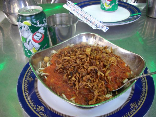 コレがコシャリ。<br />エジプトのファーストフード。<br /><br />マカロニとお米上に玉ねぎ、にんにく、トマトソースがかかっている。<br />お酢や辛いソースをかけていただく。<br /><br />マカロニとお米？と思ったが、食べたらエラくうま〜っ！！！<br />7upが懐かしいw<br /><br />100円しない。<br /><br />このお店、繁盛しすぎて1階だけだったビルを3階まで占拠しちゃったという・・・。