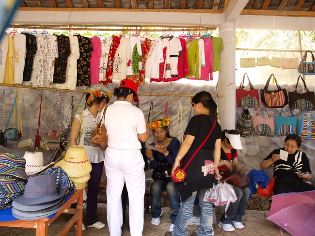 情人瀑手前の売店にて<br /><br />標高が高いせいだろう、日差しと紫外線が強い。<br />ここで後悔したのが、サングラスと夏用の日よけ効果のある帽子を持ってきていなかったことだ。<br /><br />サングラスは手に入らないが、イグサの帽子を言い値１０元を５元で買う。<br />水もここで買える。<br />女性がかぶっている花の冠は、地元のおばちゃんの手作り品だ。<br />