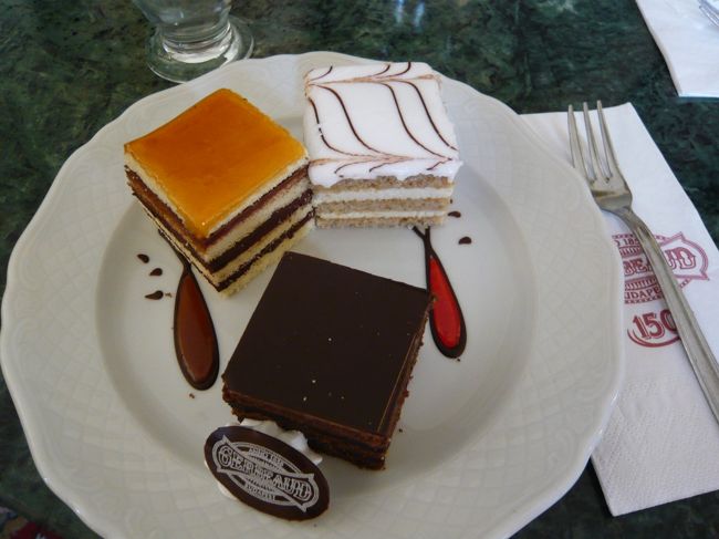 　店にはいった瞬間、ショーケースに並ぶケーキのでかさに驚愕。こ、こんなでかいケーキ、見たことない！<br />　しかし、用意されていたのは、ジェルボーの人気ケーキ３種類、ミニサイズセット、という、実に観光客向けのありがたいメニューでした。<br />　た、助かった‥‥<br /><br />　とはいえ、ひとつのサイズが日本の小さめのケーキひとつ分。<br />　そして、このみっつをあわせた大きさが、ジェルボーのレギュラーサイズひとつ分です。無理すぎる。<br /><br />　左上が、ドボシュ・トルタ。チョコクリームとスポンジを何層にも重ねて、カラメルの板（味は完璧にべっこうあめだった）がのせてあります。この板が固い！　フォークでかんかんやって、根性で割るしかない。<br />　下が、ジェルボー・トルタ。のちに、ザッハーさんが「あのカフェ・ジェルボーにおいしいケーキがあるから、あれをまねっこして作ろう」と作ったのが、有名なザッハ・トルテです。実は、ここにルーツがあったんですね〜。チョコレートずっしりのかたまりケーキでした。<br />　右上が、エステルハージー・トルタ。エステルハージー家の紋章模様のケーキです。ヘーゼルナッツ（かなあ）クリームの、比較的軽めのケーキでした。<br /><br />　みんなでぱくぱく食べながら、「うーん。おいしいけど‥‥全部、同じような味‥‥チョコレートの味しかしない」と、身もふたもない感想。唯一、エステルハージー・トルタだけが、ナッツ味なので、「これがいちばんおいしい」と絶賛ではないものの（消去法で）好評でした。<br />　うーん、やっぱり、激しく甘いんですよね〜。<br />　あのシシィが大ファンだったというケーキ屋だっただけに、期待のハードルをあげすぎてしまったか？　やっぱりケーキは日本のケーキがいちばん、わたしの舌にあっているのかも‥‥しくしく。カフェめぐりを楽しみにしてたのに！