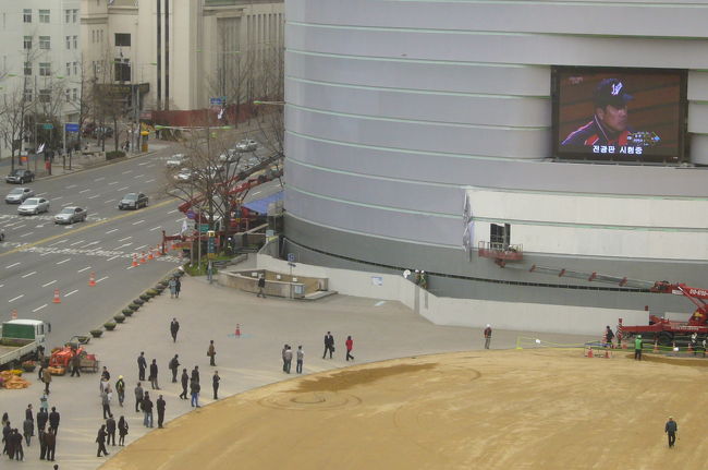 さて、今回の旅の最終日はなんと、ＷＢＣの決勝、日本ＶＳ韓国戦の日だったのです。<br />プラザホテルの窓から見える市庁前広場の巨大モニターでアメリカからの生中継です！<br />サッカーのときは真っ赤なＴシャツで埋め尽くされていたのに、野球ではこのようにチラホラとビジネスマンが足をとめる程度。韓国では野球人気はまだまだのようでした。<br />モニターに移ってるのは日本代表の原監督。<br />中継の途中で空港へ向かうツアーの集合時間になってしまいました。いちばん見たかった優勝の瞬間をリアルタイムで見れず、残念。
