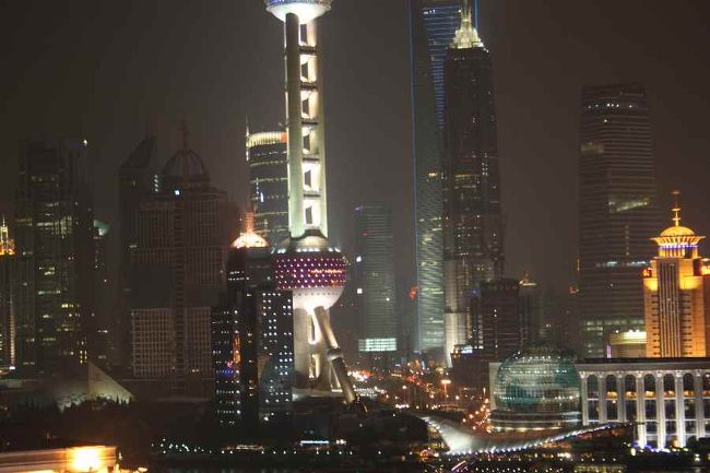 その晩、上海の夜景をホテル屋上テラスから撮影。<br /><br />東洋真珠塔には第一日目の晩に登りました。天辺まで行くのにエレベータ待ちに2時間。上海はなんと人口の多いこと！行列の先が見えません。おまけに上海人のなんとも賑やかなこと。傍から見てると気さくな感じで実に楽しそうでした。<br />ちなみに、地上まで戻るにも2時間。怪しげな観光隧道を通り、あとは徒歩でホテルに戻りました。<br /><br />さて、写真には見えませんが、空には星が瞬いおり、思った以上に空気が澄んでいて驚きました。<br />明日は本当に雨が降るのかな？<br />晴れて欲しい。<br />しかし、天体マニアの弟の情報によると、やっぱり雨だとのこと。<br /><br />ホテルの屋上（テラス）で写真撮影していると、デンマークから来たというご夫婦に遭いました。旦那さんは写真が趣味のようで、一眼レフを固定させて夜景を撮っていました。「アイル　テイク　サム　フォトズ　フォ　ユー」それから、暫く奥様とお喋りしました。「上海人は車の運転があらくて危ない。今日もあっちでも、こっちでも事故を見た」と奥さま。私も同意見。もし国際免許を発行して貰っても、上海では運転はできないと断言します。<br />夜風は清々しく、明日またこのテラスで日食を見ようと決め床に就きました。