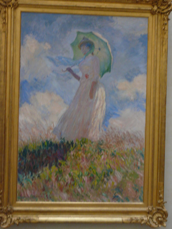 モネの有名な「日傘をさす女（左向き）」<br />モネの「日傘をさす女」は三部作でこの作品は1886年の第２作。<br />　後に自分の娘となるジュザンヌをモデルにして描かれているが。それは11年前に描かれた『日傘をさす女（散歩）』と瓜二つといわれている。<br />　もちろん、カミール・モネとジュザンヌ・オシュデの顔は当然違うだろう。しかし、後に描かれた二枚の違うべきジュザンヌの顔の部分ははっきりとは描かれてはいない。この『日傘をさす女（左向き）』ではほとんど「のっぺらぼう」と言っても良いくらいだ。だから、モネはジュザンヌをモデルにしてはいるが、亡き妻カミール・モネをその向こうに思い浮かべながら描いていたとも言われる。<br /><br /><br />