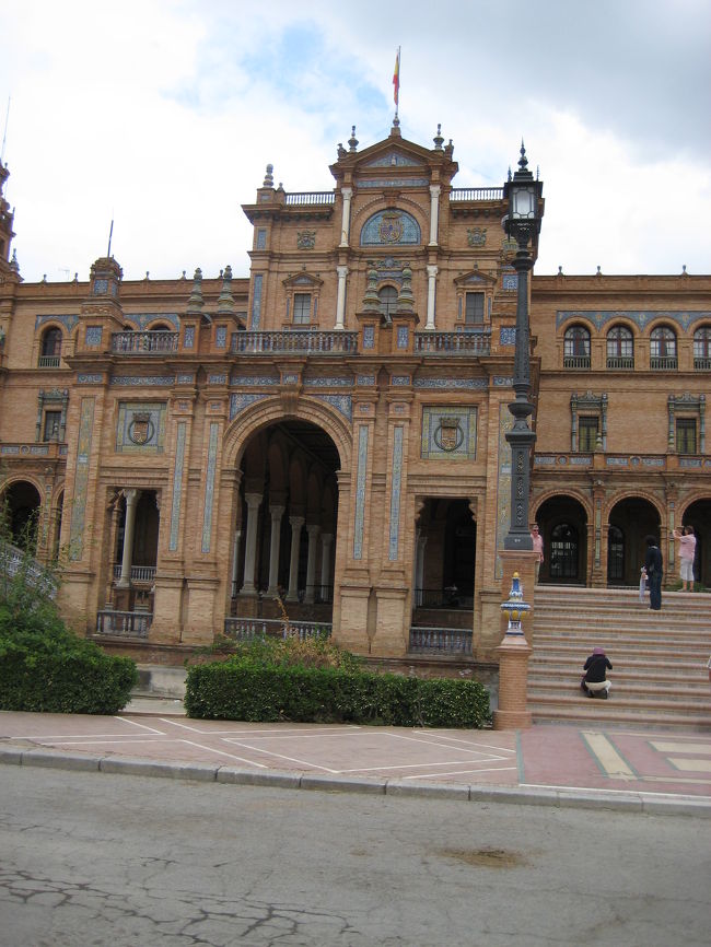 セビリアのスペイン広場。かつてサン・テルモ宮殿の庭園の一部だったマリア・ルイサ公園内にある。広場を囲む半円形の建物の下にはスペイン各県の特徴や歴史的な場面をタイルで描いたベンチが置かれている。<br />ガイドさんから、そのうちの一つグラナダ開城の図についての説明を受けた。