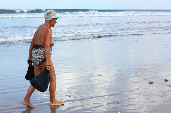 波打ち際を歩く老女。<br />