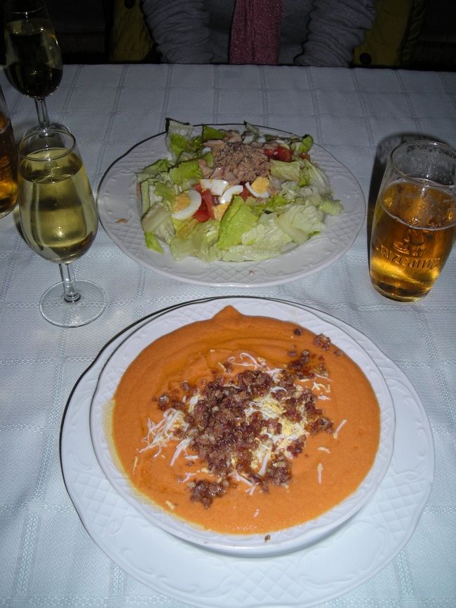 昼食。<br /><br />Meson Bodega SanBasilio<br /><br />ガイドブックに載っていた庶民的な店。<br />外から見ると立ち飲み屋のよう。たくさんのオヤジがたむろっている。<br /><br />フランス人のグループもやって来て中を覗いていたが(彼らの持っていたガイドブックにも紹介されていたようだった)、なにやら話し合った末に去っていった。<br /><br />夫が中に入って昼食が食べられるかどうか聞いてくれる。(ちなみに彼は只今スペイン語の勉強中)<br />食べられるけど、２時からだそう。<br />まだ１５分ほどあるので近くのペンチで時間をつぶす。<br /><br />そしてようやく食事！<br />立ち飲みカウンターの奥にテーブル席があった。時代を感じさせる古い造り。<br /><br />ランチセットは紙に書いたメニューがなく、店のおじさんがスペイン語で説明してくれる。前菜の「サラダかスープか？」までは理解できたものの、メインの説明には全くちんぷんかんぷん。おじさんも困り顔。<br />仲間と飲んでいた英語が話せるおじさんがやってきた。献立を英語に訳してくれようとしてくれるが、この手の説明は難しく断念。<br />メインは２品からの選択だったので、店のおじさんと客のおじさんが勝手に話し合って、両方１品ずつってことに。<br /><br />まずは前菜。<br />スープはグラナダでも食べたガスパチョ。ここのは生ハムとチーズが載っていた。グラナダの店のものよりも庶民的でお母さんの味っぽい。味もはっきりしている。おいしい！<br /><br />サラダはサラダ。こっちもドレッシングの味がはっきりしている。<br /><br />