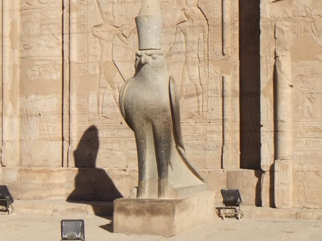 左側はこのような立派なものです。ホルスは冠をかぶっています。写真では上が切れてしまっていますが、この冠は、円筒形の筒のような冠に、とんがった形の冠がのったような形をしていて、二重王冠といいます。塔門に描かれているホルスやハトホルがかぶっているのも二重王冠です。これは、上下エジプト統一の象徴です。古代エジプトの人は、エジプトが上エジプト（ナイル川上流域）と下エジプト（ナイル川下流域）に分かれ、それをファラオが統一しているのだと考えていました。