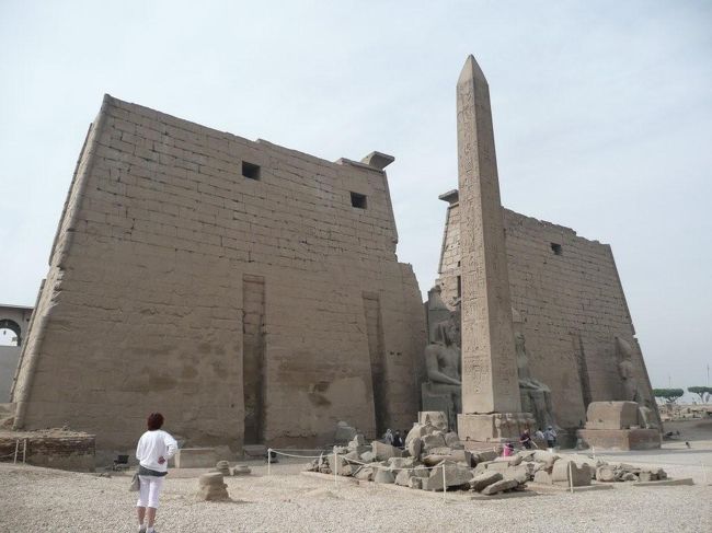 ●第1塔門とオベリスク<br /><br />エジプト中王朝時代の神殿はこの様に周囲を城壁のような壁に囲まれ、幾重にも巨大な塔門と呼ばれる入口が重なるように聖壇まで続いていた。<br /><br />この第1塔門はラムセス2世時代に建てられたものであるが、幅65メートル、高さは24メートル。今では削れて見えにくくなっているが、塔門の壁面にはラムセス2世とヒッタイトとの戦い「カディッシュの戦い」のレリーフが入れられている。<br /><br />塔門の前にはかつて2本の四角柱(オベリスク)が立っていたが、1本はムハンマド・アリが現在カイロにあるシタデルの時計と引き換えにフランスにあげてしまった。