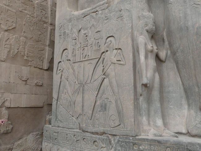 ラムセス2世坐像の足の部分には小さな像が彫刻されている。足の外側と足に挟まれた間にそれぞれ異なる像が見られるが、これらはラムセス2世の王女と王妃ネフェルタリの像。<br /><br />写真は左側の座像でり、右側の座像にも同じようにあるが、そちらの方はかなりダメージを受けており、顔がわからなくなっている。<br /><br />更に、座像の椅子部分には上下エジプト統合を象徴するハピ神のレリーフも見られる。これらは椅子の両脇、合計4枚有る。同じようなレリーフがアブ・シンベルにもあるのに注目。