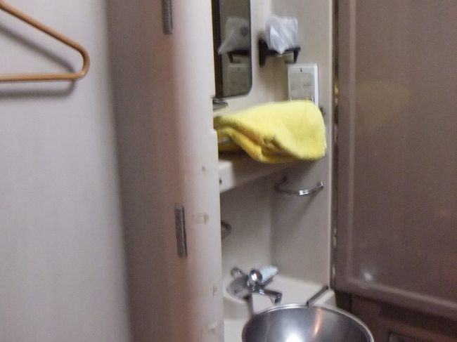 奥の左側に洗面セットがあります。洗面セットには扉があって、閉めることも出来ます。上の段には鏡があって、ペットボトルなどを固定するところもあります。黄色いタオルも用意されています。左側にはハンガーがかかっています（確か１つだけです）。