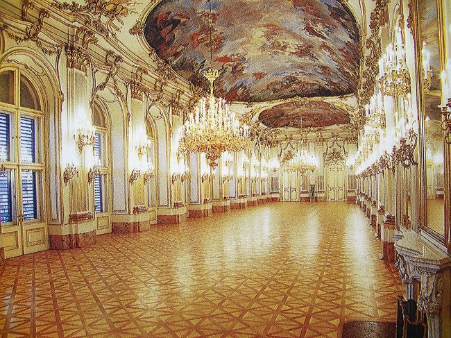 image<br />「大ギャラリー」<br /><br />長さ４０メートル、幅約１０メートルの大ギャラリーは、正面大階段と前庭を見下ろす<br />バルコニーに面しています。<br />大きな窓とこれに向かい合う鏡の数々、天井を飾るフレスコ画、<br />白と金の壁板やクリスタル製のシャンデリアで飾られ、<br />王朝時代には舞踏会、レセプション、晩餐会などが催されました。<br />第二次大戦中天井のフレスコ画に爆弾が貫通し被害を受けています。