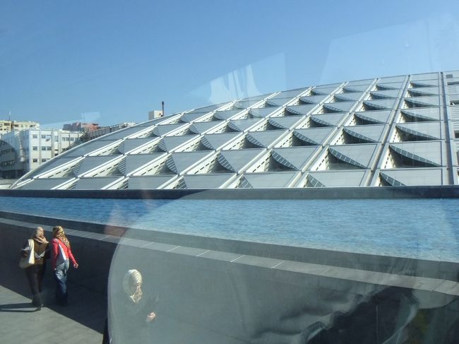 次は、アレクサンドリア図書館に向かいます。１２時４５分ころ、アレクサンドリア図書館に到着。ここはあいにく車窓観光で、バスからは降りません。右側の座席に座っているのでよく見えます。近代的な建物ですが、昔ここには、プトレマイオス１世が建てた世界最大の図書館があったのです。当時栄えていたアレクサンドリアは、訪れる外国船から本をとりあげ、元本を図書館に保管してコピーを返したそうで、世界中のたくさんの本があったそうですが、クレオパトラ時代にローマ軍の放った矢で焼けてしまいました。向こう側から見ると、円筒形の壁に世界中の言葉で文字が書かれているそうです。<br />