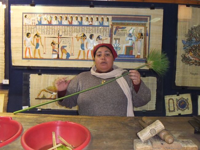 今夜のホテルはカイロではありません。深夜近くの飛行機でルクソールに飛びます。でも、ツアーですから、その前にお土産屋さんを１つ消化しなければなりません。今回のツアーでは、パピルス屋、アラバスター屋、香水屋、アクセサリー屋、じゅうたん屋の５つに強制連行されました。買い物が好きな人にはいいかもしれません。今回はパピルス屋さんです。１８時３０分到着。でも遅いので説明係の人がいません。ここでガイドさん登場(顔を出してごめんなさい。他の人の旅行記にもガイドさんは登場しているので、職業柄あきらめていただきます)。店のものを勝手に使って説明を始めます。ガイドさんが手に持っているのがパピルスという草です。この茎をちょんぎると、三角形の切り口をしています（撮影準備をしていなかったので詳しい写真はありません）。次に皮をはぎます。このガイドさん、器用で何でも出来ます。肉の部分を平たく切り、これを互い違いに網のように重ねていって、最後に圧縮機で圧縮して乾燥させればできあがり、ということのようです。肉の部分は本来柔らかくて簡単にちぎれますが、乾燥させて出来たパピルスはちぎろうとしても・・・ガイドさんの力で簡単にちぎれました。