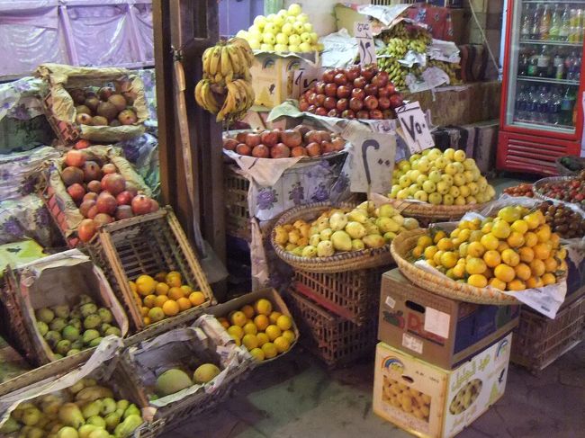 これは果物屋さんです。向こう側にバナナとリンゴのようなものは見えていますが、他の果物は日本で売っているのと少し違うように見えます。