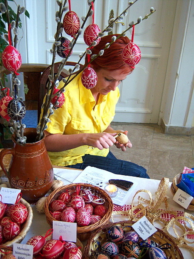 そのホールの一角では散々お土産物売り場で見た卵に絵付けをしている職人さんが！<br /><br />「写真撮らせてください！」とお願いして撮らせてもらった一枚。 <br />ろうそくの火で手元の器具の先端を焦がし？、卵に線や模様を書きこんでいます。 <br />手作業で大変だ〜〜〜！<br /><br />更にその並びには自分で卵に模様を書けるコーナーも出来ていて、600フォリントくらい出せばチャレンジ出来ました。 <br />すっごいやりたかったけど、既に親子連れでやってる人もいたし、ハンガリー語のわからない私がコツや指示を出されても理解できないので断念。 <br />うぅ〜〜細かい模様と書きこんでみたかったなぁ…。残念。 <br />楽しそうなものに惹かれるのは子供と一緒なので、ここばかりに子供が集まってたわけもわかり、私もなんだかんだでしっかり楽しんでしまいました。笑 