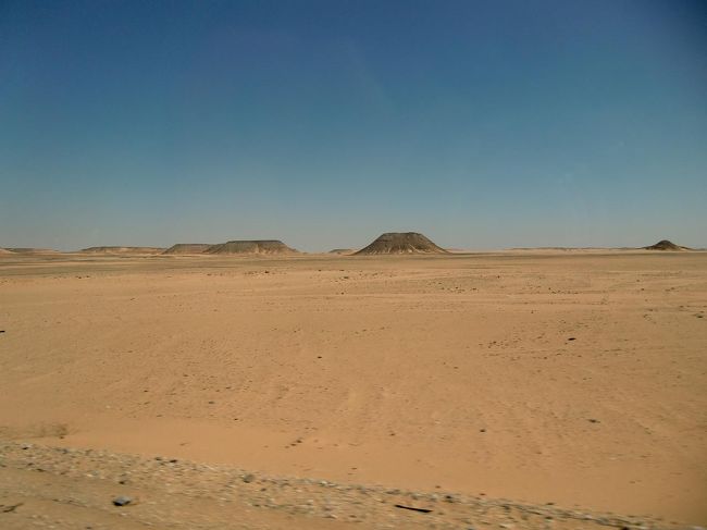 アスワン〜アブシンベル間のバス移動はコンボイ（護送船団）方式で行われている。１日の出発時間が決まっており、乗客の多いバスが先発し、空席の多いバスは後発になる。先の車が故障したら、後の車に乗客を移動させて、砂漠（写真）を横断するという。砂漠は厳しい。