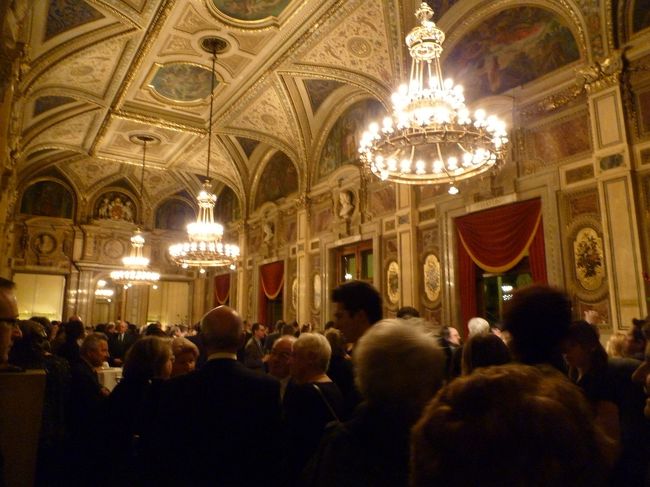 公演の幕間に、観客たちはシャンパン片手に談話しています。