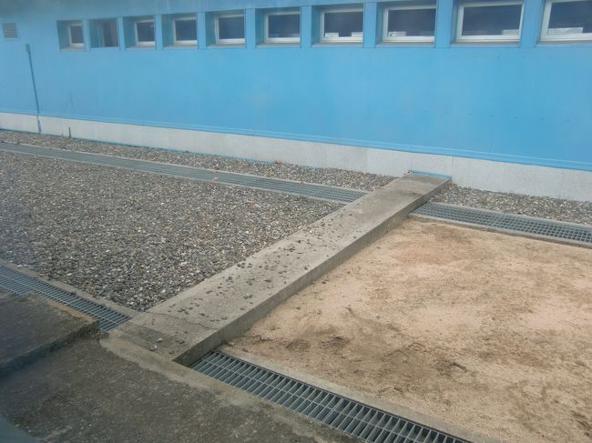 建物の外にも国境ラインがあります。<br />コンクリートラインの向こう側（砂利）が韓国、手前の砂地が北朝鮮です。<br /><br />1つ前の写真と、この写真、北朝鮮側から撮影してますね。<br />つまり、数分間私は北朝鮮に足を踏み入れたことになります。<br /><br />ガイドさんによると、これは本会議場の中だから許されること。建物の外から北朝鮮に入ると（このコンクリートラインを越える行為）、「日本人が北朝鮮に亡命しましたって大きなニュースになります。」と冗談とも本気とも取れるコメントをしていました。