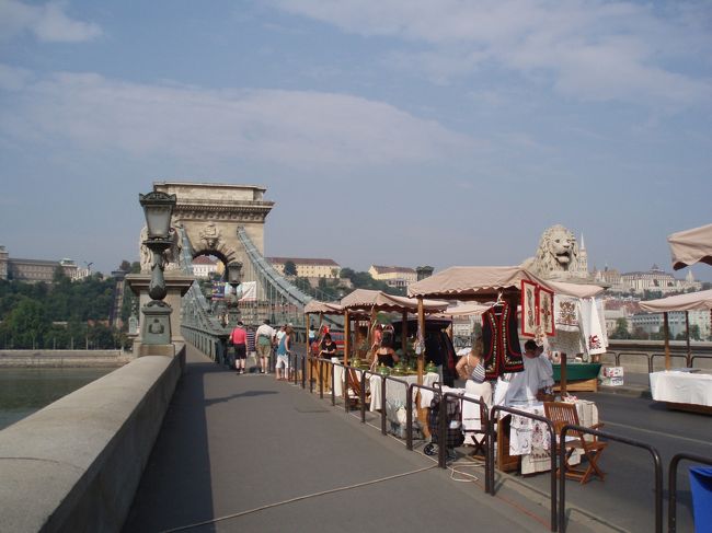 くさり橋までやってきました。<br /><br />王宮のあるブダ地区と都市機能のあるペスト地区はかつては別の街で、船が唯一の交通手段でしたが、１８４９年に初めて橋が架けられ、ハンガリーの首都“ブダペスト”が誕生したのだそうです。<br /><br />橋の建設に尽力したのは国民的英雄であるセーチェニ・イシュトヴァーン伯爵で、彼にちなんで正式には“セーチェニのくさり橋”というそうです。<br /><br />この日は土曜日のためくさり橋は歩行者天国になるようで、たくさんの露店が準備を始めていました。<br /><br />歩き続けていよいよ蒸し暑くなってきました。