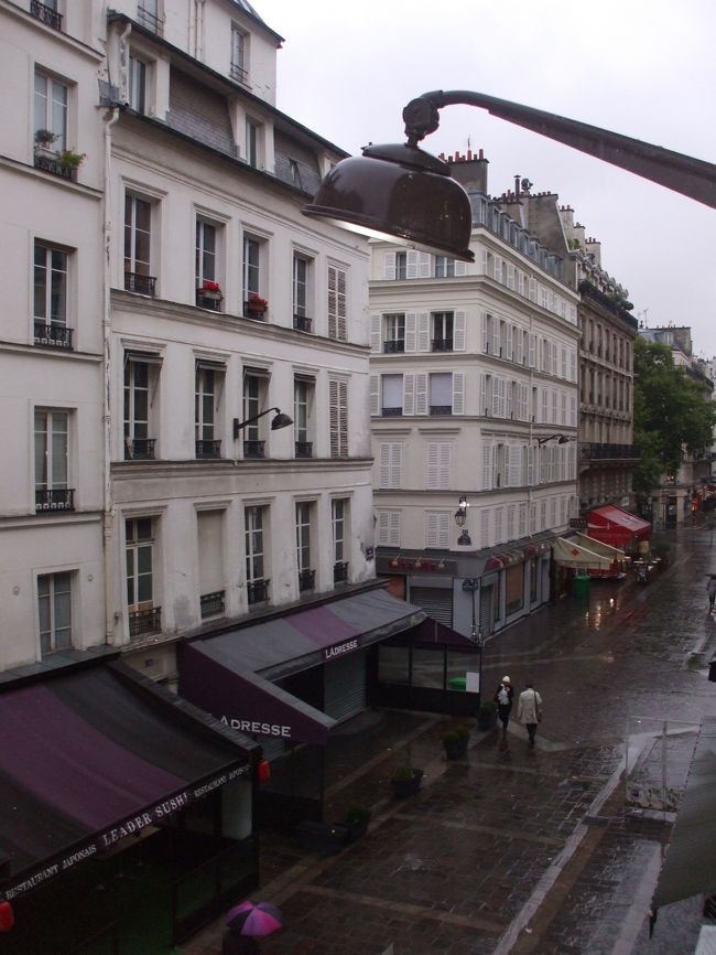 「ホテル前の通り」<br />１日歩いてくたびれた。気疲れもある。ホテルに戻ると小雨が降ってきた。近所のカフエで夕食と思ったが、熱いフロに入って休みたい。<br />近所のスーパーに買物。缶ビール３本、生ハム、チーズ、ジャム、野菜のパック、スナック、パンいろいろ、トマトジュース、牛乳、水etc。今晩の部屋でのディナーと明日朝の食料である。<br />フロ上がりのトマトジュースがメッポウうまかった。<br />パリ２日目でこれだ。まーゆっくり無理をせず観光しよう。