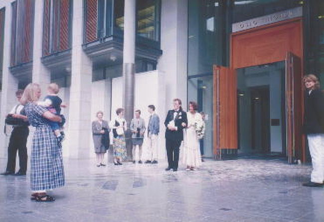 とある建物の前で新婚カップルがみんなの祝福を受けている。<br /><br />