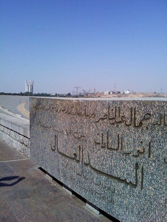 石碑にはアラビア語で「アスワンハイダム」って書いてあるのかな？<br /><br />左奥にある尖った白い建物は、記念塔。<br />ソビエトが資金提供した証に建てたらしいです。 <br />