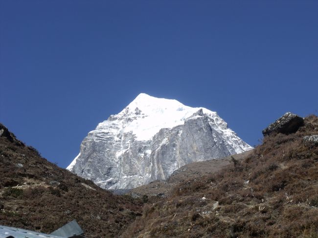 １２：４０カイラスホテルから見たカイラス。本当によく似ている。沢に沿ってずーっと下り。<br />１：１５橋の手前で一服　雲が出てきてカンテガは隠れてしまう。<br />コンデが少しだけ見える。対岸に渡る。サルガオが垂れ下がっている。<br />雨や霧が多い証拠。<br /><br />１：５０Debuche　一服きれいな新築ホテル２軒テント場あり。<br />２：２５もうすぐだからとまた一服<br />２：３０タンボチェ　２００Mも行かずについてしまった。<br />ここはすごい迫力でカンテガの横っ腹を見せてくれる。おそらく２０００Mはあるだろう。<br />時間のない人でもここまで来ればヒマラヤのすごさを体験できる。<br /><br />ここにはアルパインのメンバーが泊まっている。脇の下にペットボトルを当て、<br />ちょっと圧力をかけると、反対側の鼻づまりが取れると言っていた。<br />１２３−８６−７５若い者のような数字になった。<br /><br />一般の観光客は、タンボチェまで来るのが、せいぜいだろう。<br />カラパタールまでの行程だと「金払ってるのに何で罰ゲームみたいなことやらせるのか」と文句を言う客は確かにいそうな気はする。お金と時間とリスクを掛け合わすと最大公約数がここあたりになる。ナムチェあたりだと飛行機代もったいないと思う。ハイライト見ずに帰るって感じ<br /><br />
