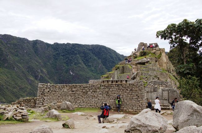 正面の壁が「神官の館」と言われる建物で、その奥に神殿があります。さらにその奥に見えるのが、このマチュピチュで最も高い場所で、日時計が設置されています。<br />