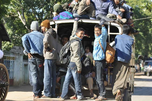 ピックアップトラックに鈴なりに乗り込み、追い抜きざま元気に手を振る少年たち。