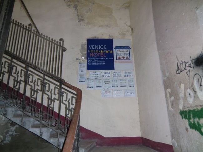 ヴェニス細川屋は４階にあります。<br />（欧米式の４階ですので、日本で言う５階になります。）<br /><br />エレベーターは古く、動いていません。<br />※いつから動いていないのか判らない程、ひどい状態でした。<br /><br />３階から４階に上がる階段に写真のようなホテルの案内板が貼ってました。<br /><br />中に入ると地元の方が２名と日本人の短期の女性担当者がみえました。<br /><br />まだ、時間があったので近隣の観光というか、ただ歩き回わってみました。<br /><br />ホテルの近くに両替屋がありましたので、明日の観光でエジプトポンドが若干不足がちでしたので、3,000円両替してみました。<br /><br />凄く換金率が良かったです。<br />日本で両替した時、１香港ドルが約20円でしたが、ここでは14円でした。<br /><br />あ〜ぁ、日本ってなんでこんなに換金率が悪いんだろう！？<br />