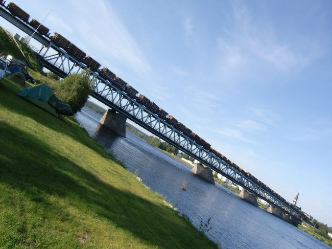 次の朝、鉄橋を轟音と共にゆっくりと、木材列車が通過します。<br />50両以上を連結しており、鉄橋の中を車が走り、上を列車が走っています。日本と逆みたい<br />　奥の△屋根はロヴァ二エミ教会です。<br />