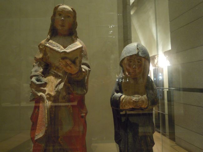 左は「本の聖女」(16世紀)とだけ書いてありました。<br />聖女バルバラのことかなあ。<br />まるで楽譜を開いて歌っているよう。<br /><br />右のおチビさんは聖母です。<br />なんだか暗くて地味。<br />ヘルメットのような頭巾をかぶってちぢこまっているのが面白い。<br />