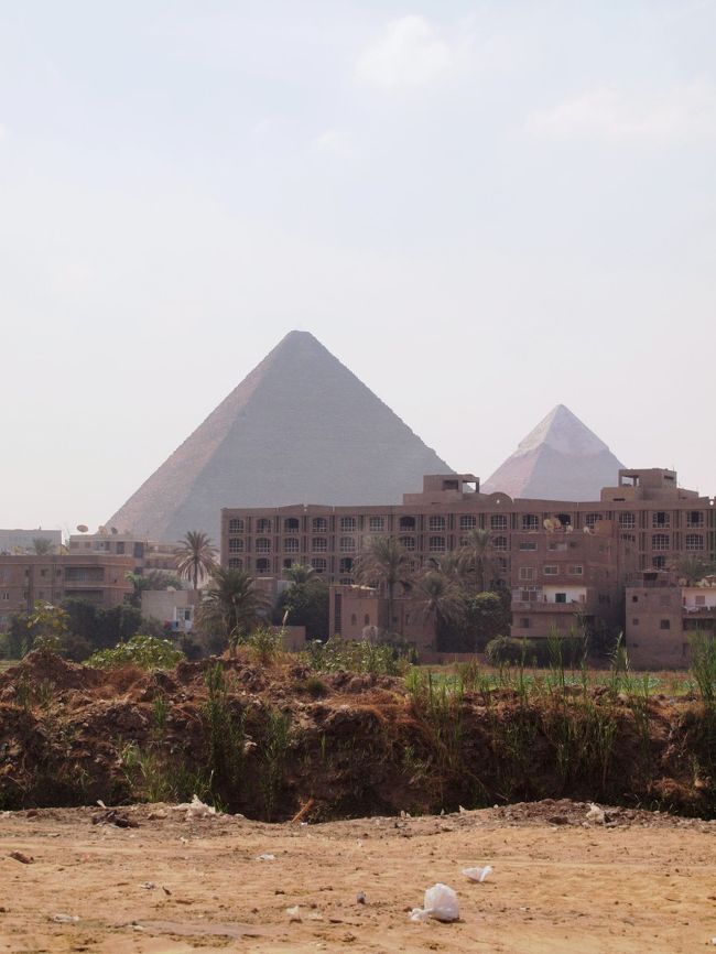 カイロ博物館を堪能したら、続いてファラオが眠るピラミッドを訪問しにギザ地区へ向かう。<br /><br />ガイドさんのお家もギザだそうで、部屋からはピラミッドが見えるそう。<br />世界遺産を部屋から毎日眺める事ができるってうらやましい。<br /><br />ギザ地区へ入ると、家々の奥にドーンと見えます見えます！<br />ピラミッド☆