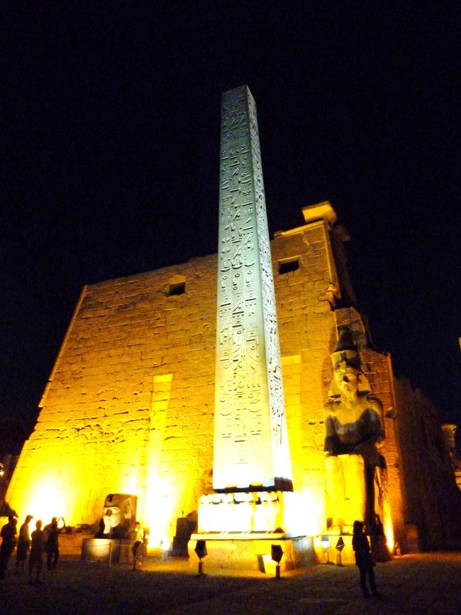 夜のルクソール神殿はライトアップされている。<br />中王国時代には神殿があったらしいが、新王国時代の第18王朝アメンヘテプ3世と第19王朝ラムセス2世が現存する神殿の大部分を作り上げたそう。<br /><br />第1塔門とその前のオベリスク。<br />もう片方のオベリスクは現在ではパリのコンコルド広場に立っている。
