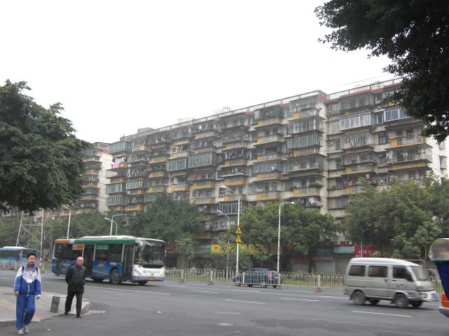 ベランダに柵の張られた団地のような住宅とジャージ姿で登校する小学生。