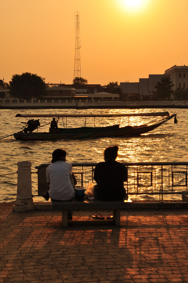 沈みゆく陽とゆっくり通り過ぎるボートを見ながら乾期の心地よい夕暮れを楽しむ老夫婦<br /><br />ちっとも夕涼みにはなりませんが、短い乾期の週末はいろんな人たちが寛ぎにやってきます。