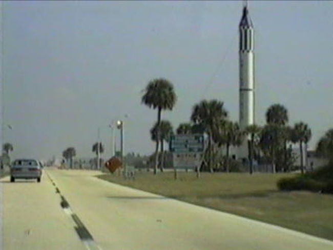 　レンタカーを借り出すのは、いくつもの書類にサインをしなければならない、面倒で気疲れする作業だけど、映画女優みたいなきれいな女性が、パンフレットを見せながら、あれやこれやとオプションを説明しつつ手続きを進めてくれます。<br /><br />　吸い込まれるような瞳に、言われるままに、イニシャルのサインを、いくつも記入して、ようやく借りられた車はフォードのコンパクトカーで、これといって特徴のない、まるで日本車のように無愛想なやつでした。<br /><br />　無意味にでかい、アメリカ的自己顕示の象徴のような車に乗って、<br />　ラジオからウルフマン・ジャックのDJががんがん流れている、<br />　そんなドライブをちょっとでも想像していたとすれば、<br />　わたしはアメリカに来るのが遅すぎたと言わなければなりません。<br /><br />　私らは、プロレスラーのような黒人のクルーから車を受けとると、そのまま東へ東へと、つまり大西洋岸に向かって突き進みました。<br /><br /><br />　アメリカ旅行の途上、フロリダ半島を三日ほどドライブ。<br /><br />　全長２３９０マイルのアメリカ国道一号線。<br />　そのどんづまりは、ヘミングウェイが最後の１ペニーまで使い果たした（と言った）キーウェスト。<br /><br />　そこで車を捨て、<br />　海の上の滑走路から飛行機で飛び立ったら、<br />　きっと自分は、アメリカの、<br />　はぐれ雲のひとつになってしまうのではないか……<br />　そんな、期待が胸を突きました。<br /><br />　でも、今はもう忘れてしまった何かの理由で、マイアミ空港までもどることにしました。　<br />　アメリカでレンタカーは、空港で借りて空港で返すのが一番簡単です。<br /><br /><br />　レンタカー屋でもらったフロリダの地図には、ディズニーワールドとかあるオーランドから、フロリダ５２８号が、真東にのびています。<br /><br />　そのずっと先に、大西洋岸に沿って皮下脂肪のように、潟が広がっていました。<br />　南北100キロにわたるホワイトホース湾です。<br />　歴とした国土をあらわすには、あまりにも大人げない地形に思え、そこはいったいどのような景色になっているのか、どうしても見てみたくなりました。<br /><br />　もあっとして、とらえどころのないの道端には、随所に田舎くさいフル−ツスタンドがあって、おばさんがいかにも普段着で店番をしています。<br />　このとき店先に並んでいたのはオレンジで、１ドルも出せば10個ほどつまった袋をもらえます。<br /><br />　「おいしいわよ。買ってきなさいよ。」<br /><br />　買ったオレンジはつぶぞろいが悪く、農家のおばさんのかわいい笑顔に、いわばだまされたカタチです。<br /><br /><br />　車は、つきぬけた青天下の一本道をどんどん進みます。<br /><br />　やがて前方に、ロケットが見えてきました。<br /><br />