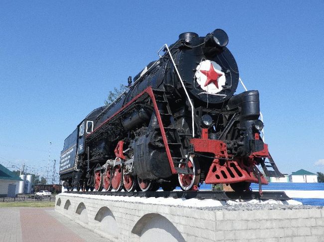 　サーシャに写真を見せながら聞いてみたところ、記念碑ではなく、どうやらこれを境にして鉄道局の管轄が変わるという目印のようであった。<br />　アチンスクとボゴトルをそれぞれ定刻に出発し、本日の最後の長時間停車となるマリンスクには定刻より2分前の17時39分に到着した。<br />　降りてみて驚いたのが、恐らく軽く30度を超えている暑さであった（33〜34度はあったかもしれない）。湿度はないが、肌に突き刺さるような暑さである。目の前を貨車が邪魔していたのでそれを迂回して駅前へ出てみると、当然のようにここにもSLが展示されてあった。<br /><br />＠ロシア号停車駅には必ずと言ってよいほどある