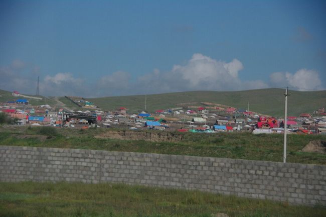 　車窓の風景その４（郊外）です。<br />　約５０分走ってきて，高い建物がなくなり，所々に観光用ではないゲルが見られるようになりました。自分ちの区画を塀で囲んでいる家も見受けられるようになり，家畜を飼うための遊牧民の冬の家などの施設かなと思っていましたが，実は，民主化後の2003年に施行された土地所有法の影響で占有区域を明示する必要からこのような姿が増えてきたらしいです。
