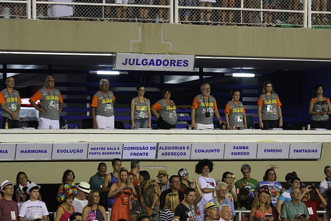 審査員の皆さんです。チームの先頭が差しかかると立ち上がり拍手で迎えます。<br />メイン会場サンボードロモでのパレードは土、日、月、火の4晩行われますが、コンテストは日、月の2晩、合計13チームで行われます。例年は12チームなのですが、今年は13チーム。そのわけは後ほど。リオのサンバチームはリーグ制になっていて、日、月の13チームは1部の精鋭チームです。チームと書きましたが、正しくはEscola de samba (エスコーラは学校の意味）。学校というより地域に根ざしたチームという感じだそうで、リオには数百のエスコーラがあるとのこと。土や火曜日は2部や3部のチームのパレードが行われるそうです。