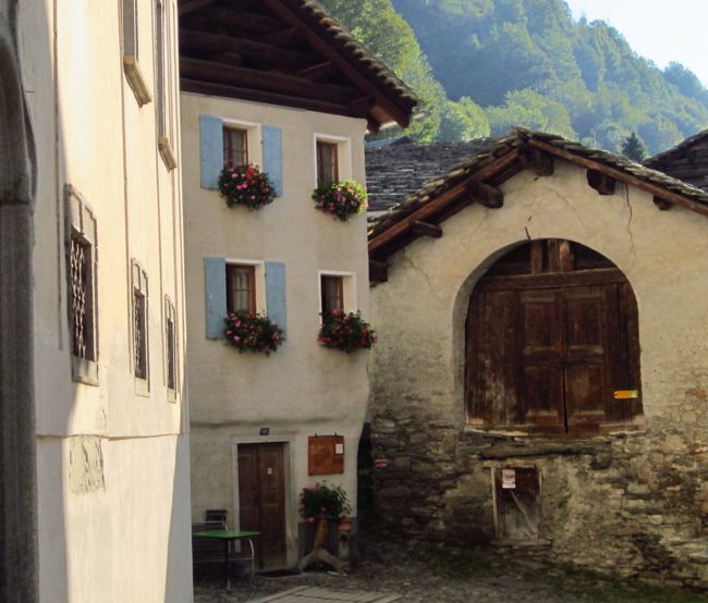 家の線が直線ではなく、自然の曲りが建物の感じを柔らかくしている。そして、物置小屋か穀物蔵かわからないが、建物正面の木製の扉とひびが入っていた漆喰は風雪に耐えてきた存在感がある。<br />建物の古さとは対照的に、窓からはスイスの家らしい鉢植えの花が飾られている。