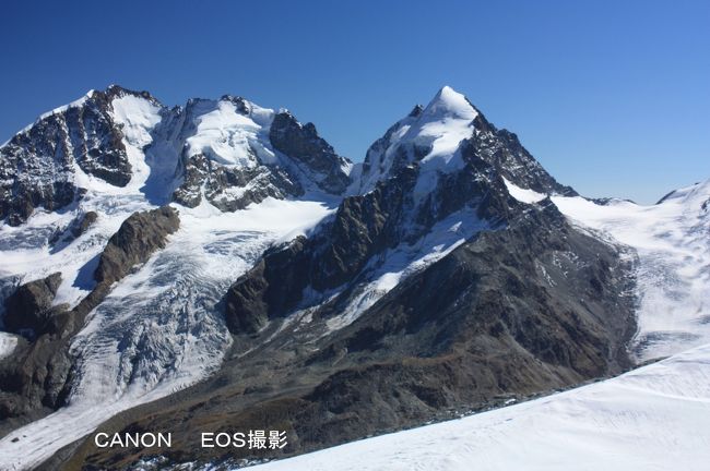 ムルテール中間駅でロープウェーを乗り換え、コルヴァッチ展望台（3303ｍ）に到着。展望台に出て目の前に現れた迫力ある4000ｍの山並みを撮影。<br />左側の山がベルニナの最高峰ピッツ・ベルニナさんで右側の三角形に尖った山がピッツ・ロゼック山である。