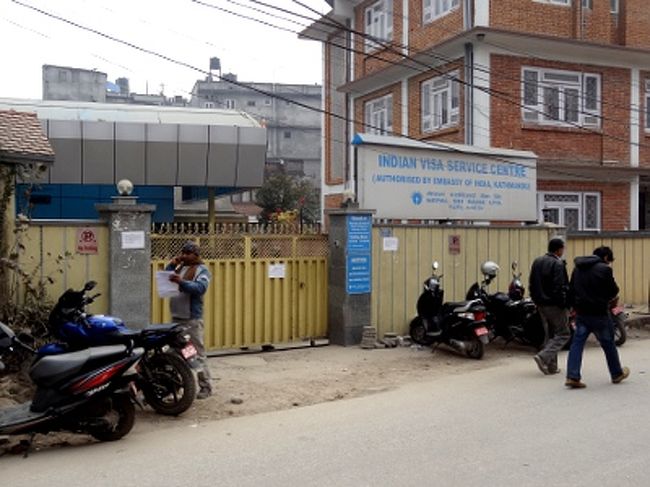 [基本ルーチン #1 - 早朝から並ぶ]<br /><br />　さて、前日までにオンライン申請して必要書類を揃えたところで、ビザセンター(写真)に突撃です。カトマンズのビザセンターは、インド大使館の手前、イギリス大使館の向かい側にあります。具体的な場所は歩き方の地図を参照して下さい。タメルから歩いて15分ほどの距離にあります。<br /><br />　ここカトマンズでは、インドのSBI銀行がビザ・サービスの業務を請け負っています。ということは、窓口の職員は、大使館員ではなく銀行員？　土日はきっちり休みます。